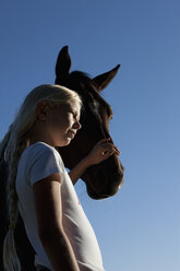 Girl petting horse muzzle under blue sky - FSIF03317