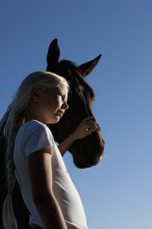 Mädchen streichelt Pferd Schnauze unter blauem Himmel - FSIF03317