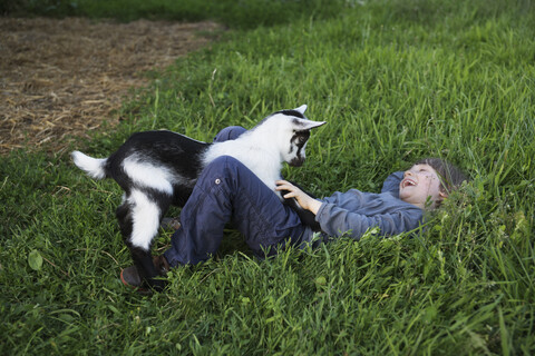 Glückliches Mädchen spielt mit Ziege im Gras, lizenzfreies Stockfoto