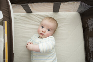 Overhead portrait of cute baby boy lying on mattress in pack n' play at home - CAVF49105