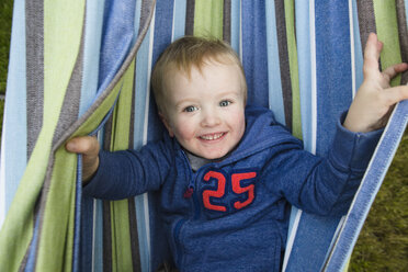 Overhead-Porträt eines fröhlichen Jungen in einer Hängematte im Hinterhof - CAVF49107