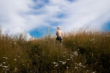 Rückansicht eines Jungen ohne Hemd, der auf einem grasbewachsenen Feld gegen einen bewölkten Himmel läuft - CAVF49109