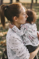 Mother carrying daughter while standing at park during autumn - CAVF49113