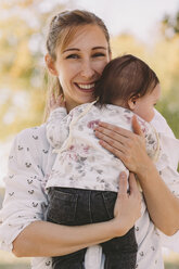 Porträt einer glücklichen Mutter, die ihre Tochter im Herbst in einem Park auf dem Arm hält - CAVF49114