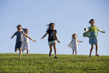 Happy siblings running on grassy field against clear blue sky at park - CAVF49116