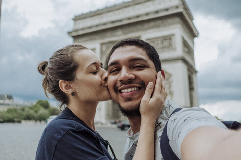 Porträt einer Freundin, die ihren lächelnden Freund vor dem Arc de Triomphe in der Stadt küsst - CAVF49135