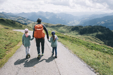 Rückansicht einer Mutter mit ihren Töchtern, die auf einer Bergstraße gegen einen bewölkten Himmel laufen - CAVF49139