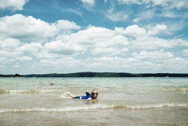 Boy wearing swimming goggles while lying in sea against cloudy sky - CAVF49141