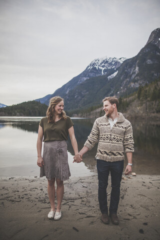 Lächelndes junges Paar in voller Länge, das sich am Seeufer des Silver Lake Provincial Park an den Händen hält, lizenzfreies Stockfoto