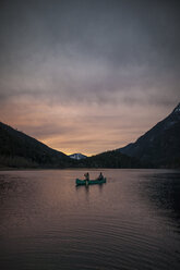 Blick aus der mittleren Entfernung auf ein Kanupaar auf dem See vor dem Hintergrund der Berge und des Himmels während des Sonnenuntergangs im Silver Lake Provincial Park - CAVF49163