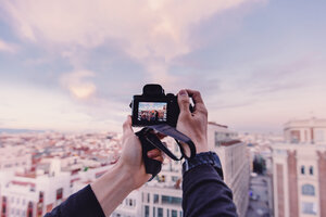 Abgeschnittene Hände eines Mannes, der bei Sonnenuntergang eine Stadtlandschaft gegen den Himmel fotografiert - CAVF49179