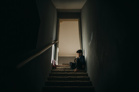 Low angle view of boy sitting on steps at doorway in home stock photo