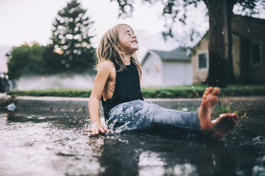 Happy girl sitting on wet street during rainy season - CAVF49209