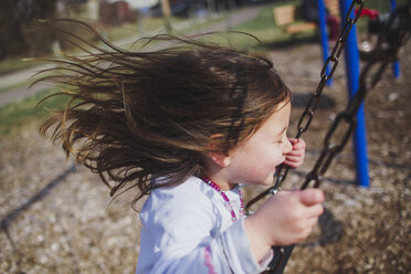 Side view of playful girl swinging at playground - CAVF49212