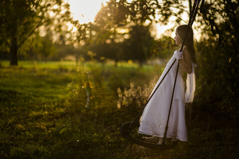 Side view of girl in dress swinging at park during sunset stock photo