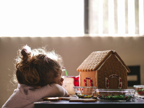 Mädchen ruht sich bei einem Lebkuchenhaus auf dem Tisch zu Hause aus, lizenzfreies Stockfoto