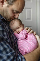 Father kissing newborn daughter while sitting at home - CAVF49223