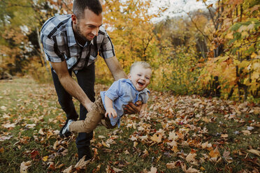 Vater spielt mit seinem Sohn auf einer Wiese im Wald im Herbst - CAVF49227