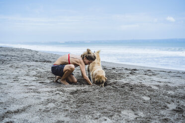 Frau und Labrador Retriever in voller Länge beim Graben am Strand - CAVF49238