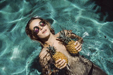 Draufsicht auf eine hemdsärmelige Frau, die eine Sonnenbrille trägt und ihre Brüste mit Ananas im Sommerschwimmbad bedeckt - CAVF49239