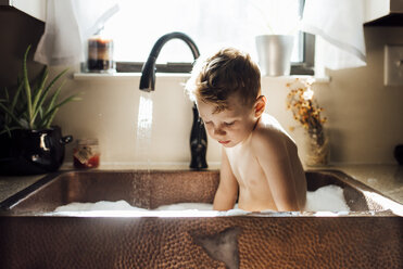 Shirtless boy taking bath while sitting in sink at home - CAVF49251