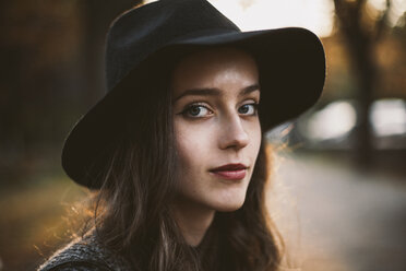 Close-up portrait of woman wearing hat while sitting at park during sunset - CAVF49262