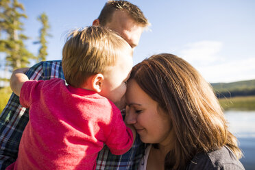 Liebevoller Sohn, der den Kopf der Mutter berührt, während er vom Vater gegen den See getragen wird - CAVF49279