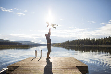 Volle Länge des spielerischen Vater wirft Sohn in der Luft gegen See und Himmel während des sonnigen Tages - CAVF49282