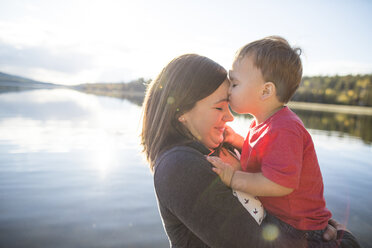 Son kissing mother on forehead against lake - CAVF49284