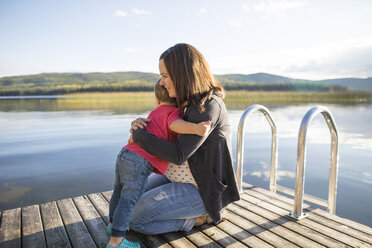 Liebender Sohn umarmt schwangere Mutter auf Holzsteg über See - CAVF49286