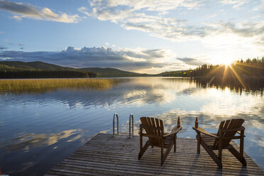 Leere Stühle auf Holzsteg über See gegen bewölkten Himmel bei Sonnenuntergang - CAVF49287