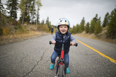 Porträt eines niedlichen, fröhlichen kleinen Jungen, der auf einer Landstraße Fahrrad fährt - CAVF49289