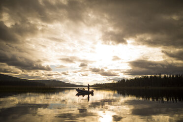 Entfernte Ansicht von Vater und Sohn in einem Boot auf dem See gegen den bewölkten Himmel bei Sonnenuntergang - CAVF49292