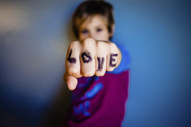 Nahaufnahme eines Mädchens, das an einer Hauswand stehend seine Finger mit einem Liebestext zeigt - CAVF49301