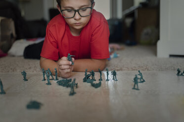 Junge spielt mit Miniatur-Plastiksoldaten auf dem Boden zu Hause - CAVF49309