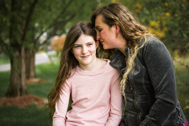 Close-up of mother whispering to daughter while sitting at park - CAVF49320