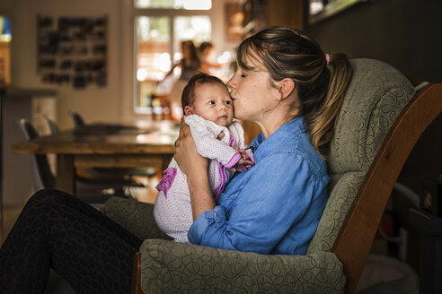 Side view of mother kissing daughter while sitting on sofa at home - CAVF49328