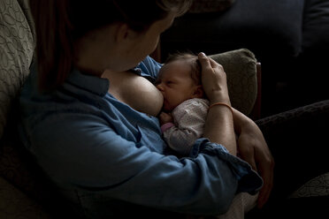 High angle view of mother breastfeeding newborn daughter while sitting on sofa at home - CAVF49329