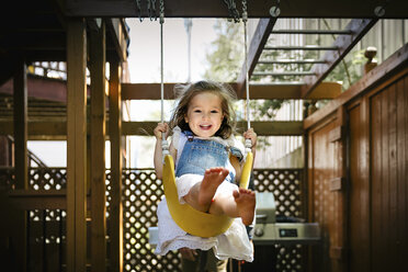 Full length portrait of happy girl swinging in backyard - CAVF49333