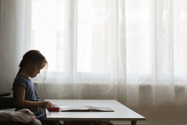 Seitenansicht eines Mädchens, das zu Hause auf einem Tisch am Fenster Klavier spielt - CAVF49338