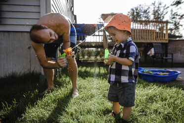 Verspielter Vater sprüht Wasser mit Spritzpistolen auf seinen Sohn, während er im Garten spielt - CAVF49339