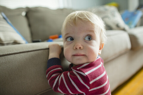 Nahaufnahme eines süßen kleinen Jungen, der wegschaut, während er zu Hause auf dem Sofa sitzt, lizenzfreies Stockfoto