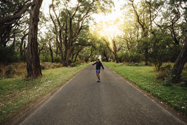 Man skateboarding on road amidst trees in forest against sky during sunset - CAVF49371