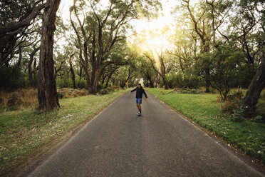 Mann fährt Skateboard auf der Straße inmitten von Bäumen im Wald gegen den Himmel bei Sonnenuntergang - CAVF49371