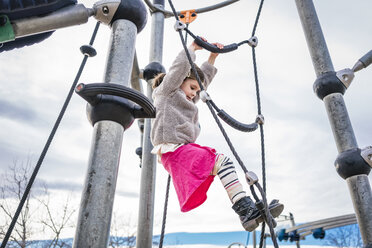 Niedriger Winkel Blick auf Mädchen klettern auf Seil gegen bewölkten Himmel auf dem Spielplatz - CAVF49375