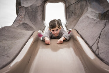 Low angle portrait of playful girl sliding at playground - CAVF49378