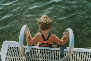 High angle view of girl wearing swimwear while sitting on ladder in lake - CAVF49390