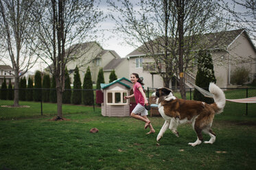 Glückliches Mädchen spielt mit Hund auf grasbewachsenem Feld im Hof - CAVF49393