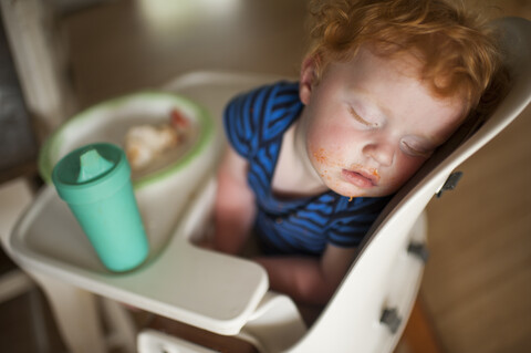High angle view of cute baby boy with food and drink sleeping on high chair at home stock photo