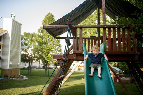 Glücklicher Babyjunge schreit beim Rutschen auf dem Hof, lizenzfreies Stockfoto